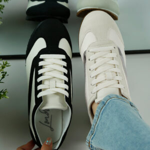 A pair of black and white sneakers displayed with laces, one held in hand and the other on a reflective surface.