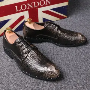 Brown dress shoes with a crocodile pattern and black soles placed on a gray surface.