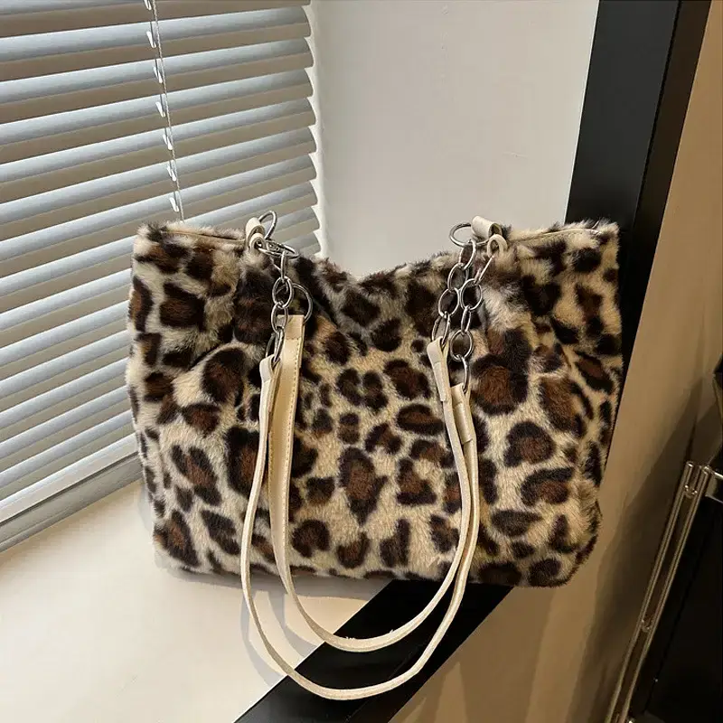 A leopard print faux fur handbag with white straps. Leopard print handbag made of faux fur with white straps displayed on a surface.