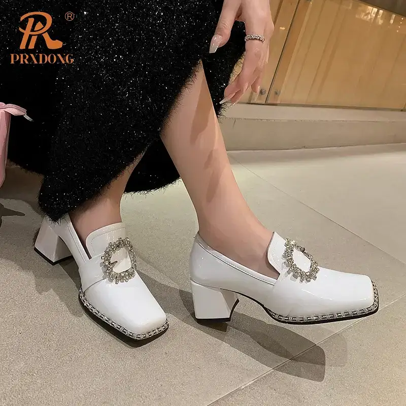White heeled shoes with a decorative buckle detail. White heeled shoes featuring a decorative buckle on the front, worn by a person in a black outfit.