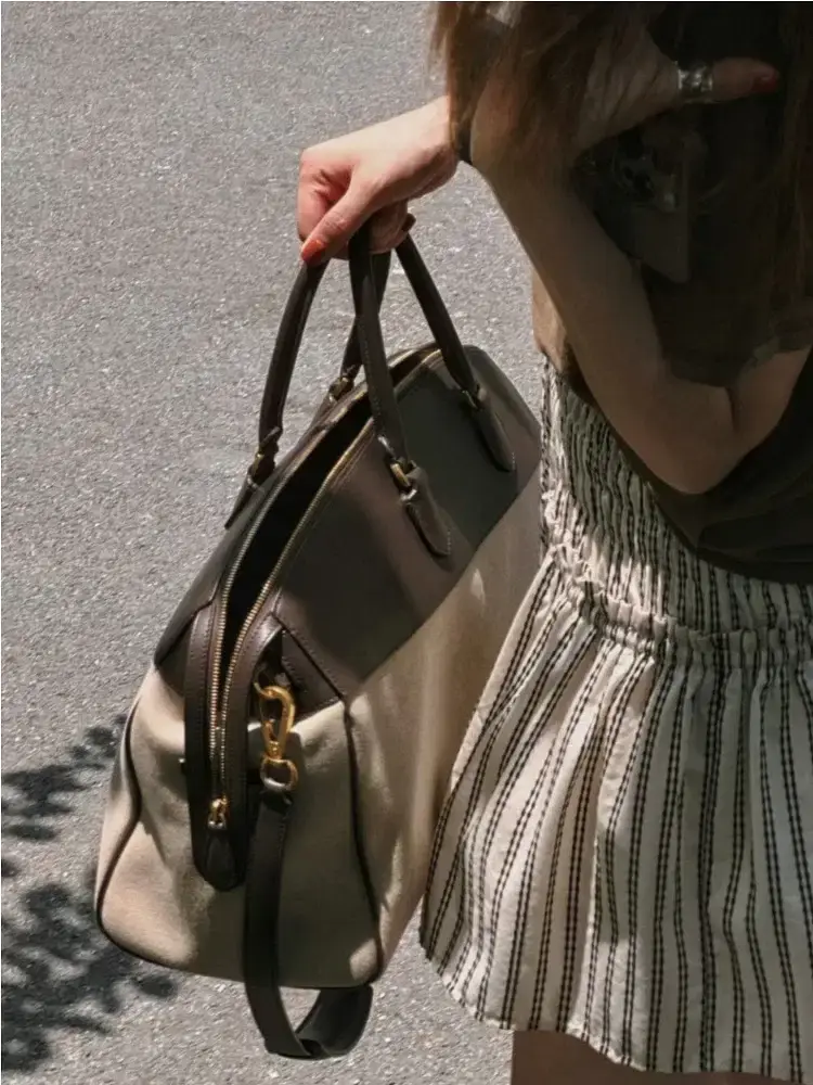 A beige and brown handbag held by a person in a striped skirt. A person holding a beige and brown handbag while wearing a striped skirt.