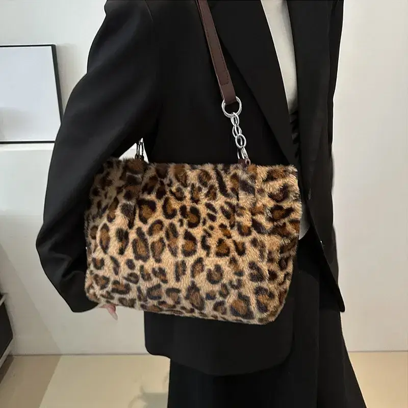 A leopard print handbag with a chain strap. A leopard print fur handbag held by a person wearing a black outfit.