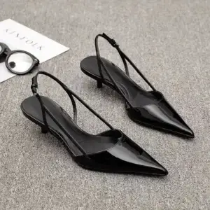 A pair of black patent leather slingback heels with a pointed toe and a low heel.