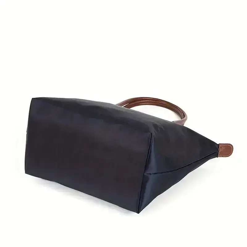 A navy blue tote bag featuring brown leather handles. Navy blue tote bag with brown leather handles, viewed from the side.