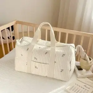 Quilted white travel bag with handles placed on a bed in a light-colored room.