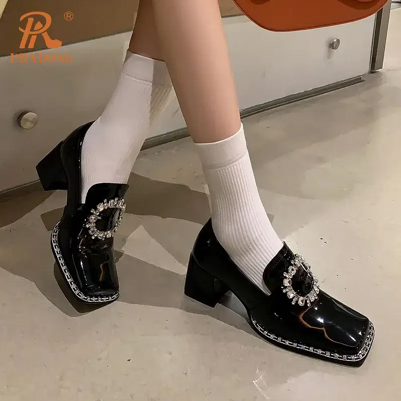 Black patent leather heeled shoes with a decorative buckle. Black patent leather heeled shoes featuring a decorative buckle and worn with white socks.