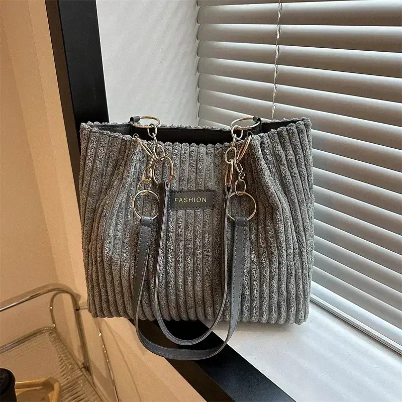 A gray ribbed handbag featuring chain straps. Gray ribbed handbag with chain straps and a label that says 'FASHION'.