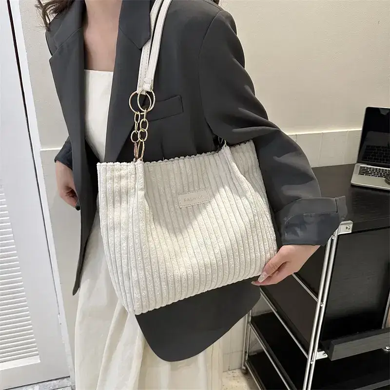 A white ribbed handbag held by a woman in a gray blazer. A woman wearing a gray blazer holding a white ribbed handbag with a chain strap.