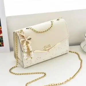Cream handbag featuring a chain strap and a decorative bow with pearls on the front.