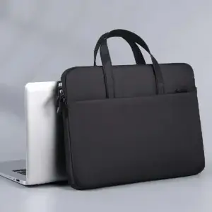 Black laptop sleeve with handles placed behind a silver laptop on a gray surface.