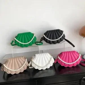 Five shell-shaped handbags in green, black, white, pink, and beige with pearl accents displayed on a shelf.