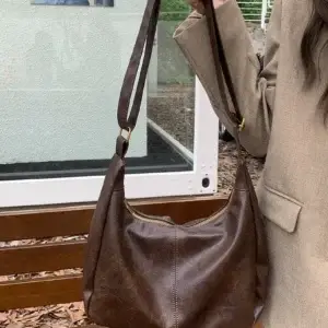 A brown leather shoulder bag held by a person wearing a beige blazer.
