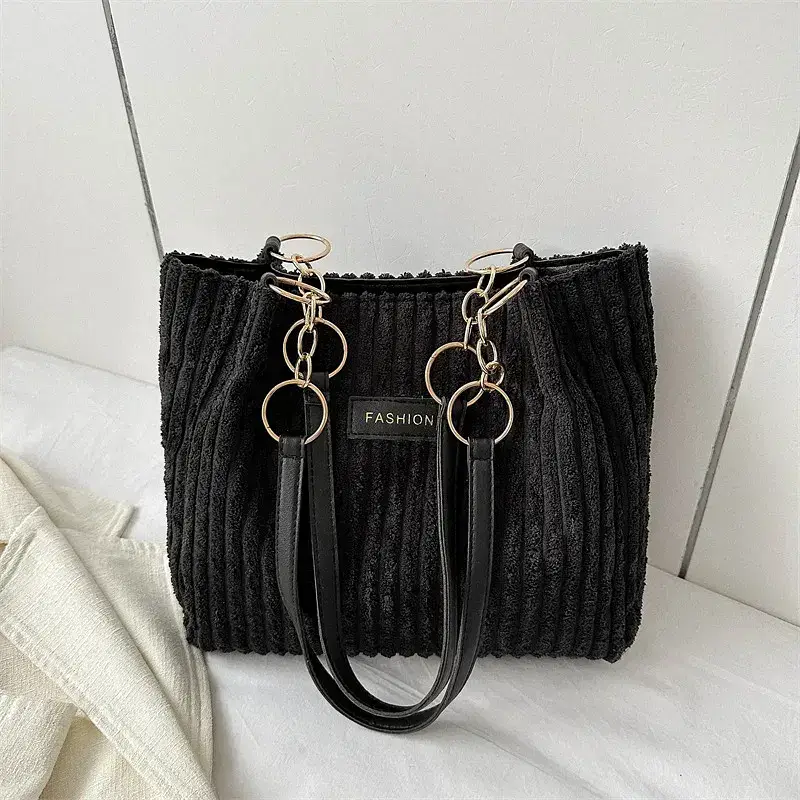 A black ribbed handbag with chain details and leather straps. Black ribbed handbag featuring gold chain accents and dual handles.