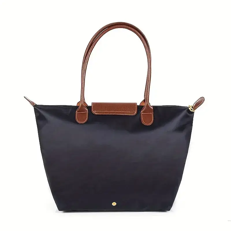 A navy blue tote bag with contrasting brown leather handles. Navy blue tote bag featuring brown leather handles and a gold button detail.
