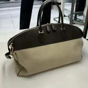 Beige handbag with brown leather accents and dual handles placed on a flat surface.