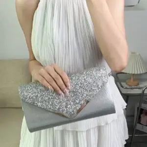 A person holding a silver glitter clutch bag with a pleated dress in the background.