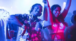 Two individuals dancing at a nightclub with headphones on, surrounded by colorful lighting.