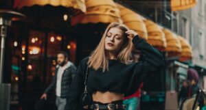 Woman with long hair wearing a black crop top and high-waisted pants, walking outdoors.